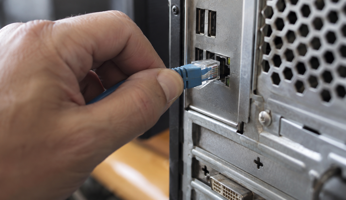 Close shot of a hand unplugging an ethernet cable from the back of a desktop computer tower