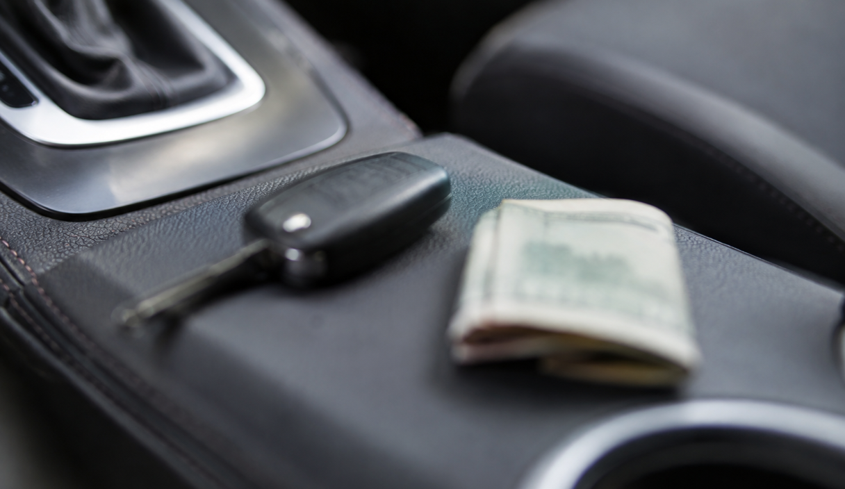 A car key and a folded paper bill lying on a car's center console in soft daylight